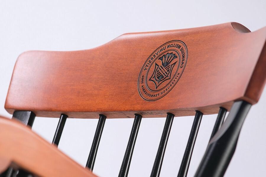 A close up picture of the top of a wooden chair, with the CMU logo in the top arch